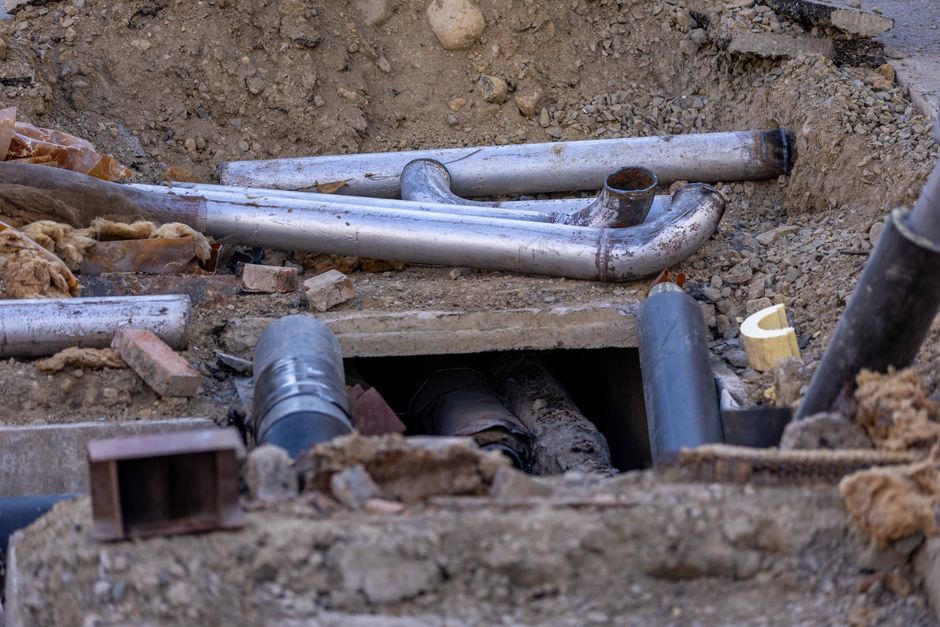 Rörinstallation på byggarbetsplats med stålrör i schakt och markarbete.
